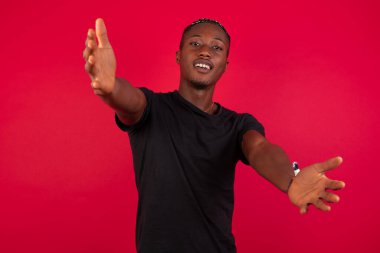 Kırmızı arka planda siyah tişört giyen Afro-Amerikalı adam ellerini gösteriyor.