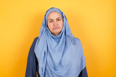 Hüzünlü, orta yaşlı, tesettürlü Müslüman kadın kaşlarını çatmış yukarı bakıyor, elleri aşağıda konuşmaktan rahatsız oluyor, yorgun ve gitmek istiyor.