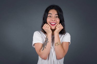 Mutlu bir kadının stüdyo çekimi, keyifli bir ruh halinde, çene altında el ele tutuşur. Ertesi gün için arkadaş fikrini sever. Gri duvarda izole olur. Pozitif duygular.