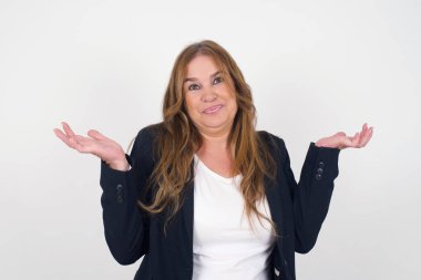 Güzel orta yaşlı kadın şüphe ifadesi, kafa karışıklığı ve merak, belirsiz gelecek omuz silkiyor, gri duvara karşı duruyor..