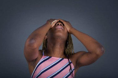 Şok olmuş genç Afro-Amerikalı kadın şık giyinmiş, yüzüne el ele tutuşmuş, gözleri kapamış, umutsuzluk ve hüsran içinde çığlık atarken gri arka planda duruyor. 