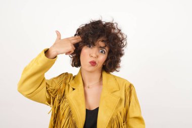 Mutsuz sarışın genç kadın silah atışı taklidi yapıyor intihar jesti yapıyor iki parmağını şakakların üstünde tutuyor günlük kıyafetleri giymiş şaşkın ifade içeride duruyor..