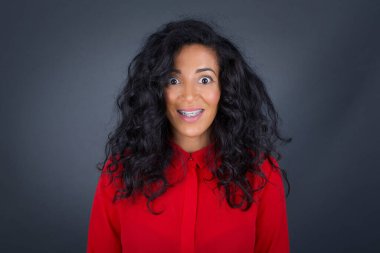 Kıvırcık saçlı, kırmızı tişörtlü, genç, güzel, esmer bir kadın. Geniş, beyaz bir gülümsemesi var. Arkadaşlarıyla tanışacağı için heyecanlı..