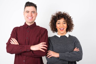  Kollarını kavuşturup gülümseyen çift duvara yaslanmış kameraya bakıyor. Pozitif kişi.