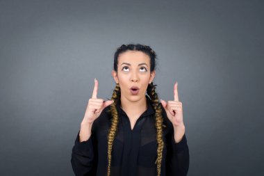 Güzel, zarif bir kadının portresi izole edilmiş arka planda şaşkın şaşkın bakıyor ve parmaklarıyla garip bir şey gösteriyor..