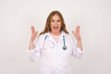 Başarı, başarı konsepti. Medikal üniforma giyen neşeli, olgun, beyaz doktor kadın ellerini kaldırıyor, tıp üniforması giyiyor, gözleri mutluluk dolu, büyük başarılarını kutluyor..