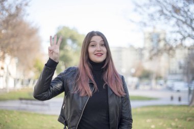 Genç ve güzel bir kadın parkta üç parmağını gösteriyor.