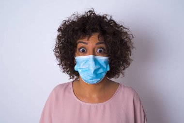 Yüz maskesi takan ve günlük giysiler giyen bir kadın beyaz stüdyo arka planında yalnız kalmaktan korkuyor.