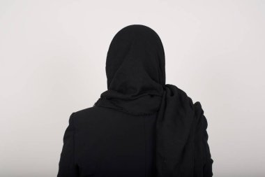 Siyah tesettürlü Müslüman bir kadının gri duvarın önünde duruşu. Stüdyo Çekimi.