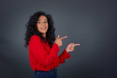 Kıvırcık saçlı, kırmızı tişörtlü, ağzı açık, neşeli ve şaşkın bir ifade takınan çekici, genç esmer kadın içeride inanılmaz bir şey gösteriyor. Reklam kavramı.