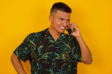 Yaşam Tarzı Konsepti - Arkadaşlarıyla cep telefonunda konuşan başarılı İspanyol adamın portresi. Sarı pastel stüdyo arka planı. Boşluğu Kopyala.