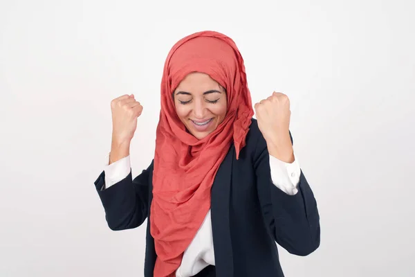 美しいイスラム教徒の女性は黒いブレザーとヒジャブを着て 彼女の成功と勝利を喜びで彼女の拳をクレンチしています 彼女の目標と目標を達成するために幸せな髪の束を持つ幸運な女性 ポジティブな感情 — ストック写真