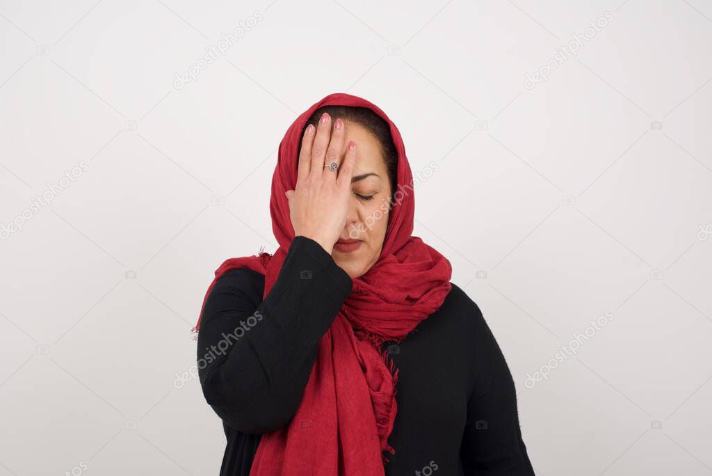 Frustrated mature muslim woman  holding hand on forehead being depressed regretting what she's done having headache. 