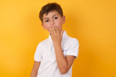 Sarı duvara karşı eli ağızda tatlı bir çocuk.  