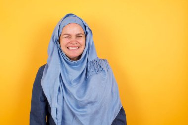 Orta yaşlı, tesettürlü tatlı Müslüman kadın mutlu bir ifadeyle gözlerini kırpıyor. Yüz ifadeleri ve insanların duygu konsepti.
