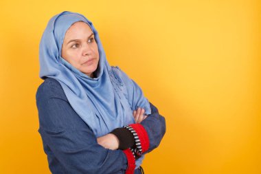 Orta yaşlı, tesettürlü, üzgün bir müslüman kadın görüntüsü. Kapalı bir odada kolları bağlı duruyor.. 