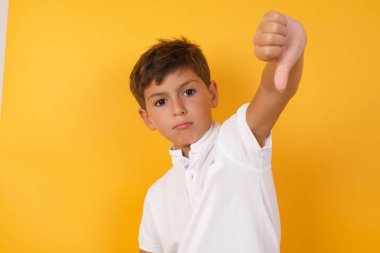 Başparmağı sarı duvara dayalı sevimli bir çocuk.  