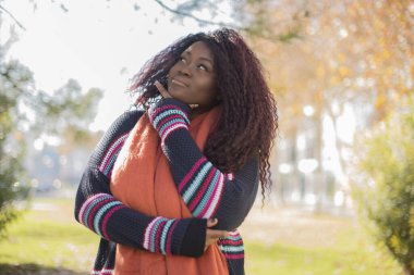 Güz parkında uzun saçlı, renkli süveter giyen güzel Afrikalı Amerikalı kadın.  