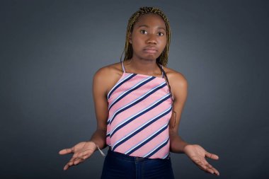 Şaşırmış ve cahil Afrikalı Amerikalı kadın kollarını açmış gri stüdyo arka planında omuzlarını silkiyor.