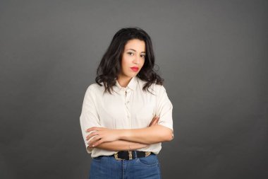 Kollarını kavuşturmuş güzel esmer kadın. Gri arkaplanda duruyor. 