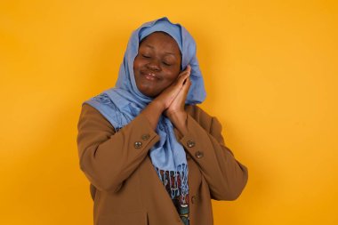 Rahatla ve uyu. Yorgun, güzel, Afro-Amerikan Müslüman bir kadın. Gözleri kapalı, yastık gibi avuçlarına yaslanmış, yorgun düşmüş gibi yapıyor. Sarı arka planda duran rüyalar görüyor. Uyuma hareketi.