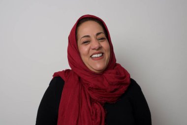 Neşeli bir kadın iyi bir şakaya gülüyor ve eğleniyor ya da gri duvarda dikilerek günlük kıyafetler giyiyor. Uzun saçlı mutlu kadın içeride poz veriyor. Stüdyoda poz veren başörtüsü takan orta yaşlı bir Arap kadın.