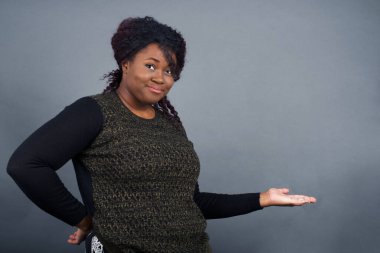 Güzel Afro-Amerikan kadınının portresi. Gri arka planda, kolları açık, hoş geldin jesti yapıyor..