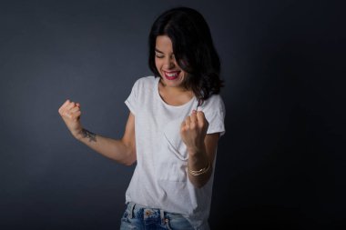 Kafkasyalı esmer kadın başarısını ve zaferini sevinçle kutluyor ve yumruklarını zevkle sıkıyor. Tüylü, şanslı kadın hedefine ve hedeflerine ulaştığına seviniyor. Olumlu duygular, duygular. 