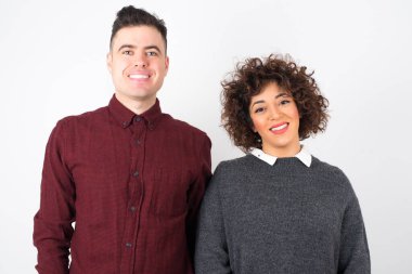 Güven ve iş kavramı. Çekici ve başarılı genç bir çiftin portresi, beyaz duvarın önünde duran kendinden emin bir ifadeyle geniş bir gülümseme ile..