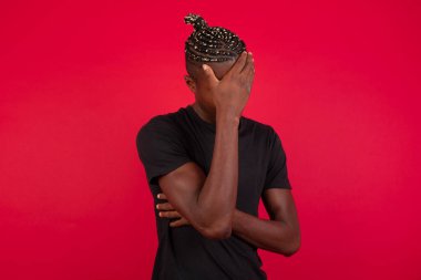 Havalı saç kesimi olan yakışıklı bir adamın kapalı bir portresi, günlük kıyafetler giyen, gülümserken facepalm jestleri yapan, arka planda duran, aptalca durumlardan etkilenen,.