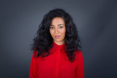 Stüdyoda, kıvırcık saçlı, kırmızı tişörtlü güzel bir kadının hoş bir gülümsemeyle kameraya bakarken gri, boş bir fotokopi duvarına poz verirken ki görüntülerini kapatın. 