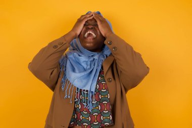 Şok olmuş Afro-Amerikan Müslüman kadın şık giyinmiş ellerini yüzüne koyup gözlerini kapatıyor ve umutsuzluk ve hüsran içinde çığlık atıyordu..