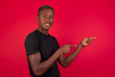 Kırmızı arka plan noktaları üzerinde siyah tişört giyen, ağzı açık, neşeli ve şaşırmış yüz ifadesi olan olumlu, Afro-Amerikalı bir adam içeride inanılmaz bir şey gösteriyor. Reklam kavramı.