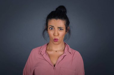 Gri arka planda sabırsız ifadesi olan güzel, genç bir kadın suratını buruşturuyor. 