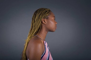 Gri duvarda dikilen Afrikalı Amerikalı genç bir kadının profil portresi. 