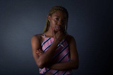 Düşünceli gülümseyen Afro-Amerikan kadının portresi elini çenesinin altında tutuyor ve doğrudan kameraya bakıyor.