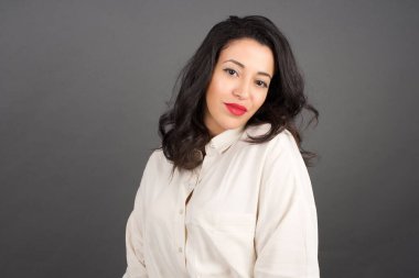 Güzel esmer kadın, sıradan bir şekilde gülümsüyor. Gri arkaplanda duruyor. 