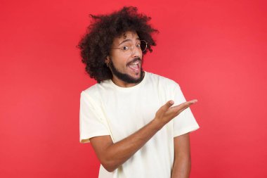Kızıl duvarda bir şey gösteren afro saçlı genç adam.   