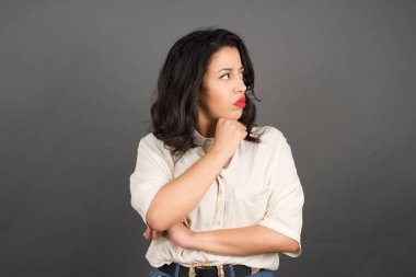 Güzel esmer kadın başka tarafa bakıyor. Gri arkaplanda duruyor. 