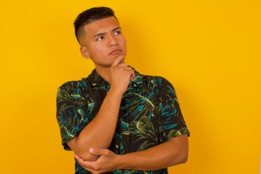 Düşünceli gülümseyen İspanyol erkeğin portresi elini çenesinin altında tutuyor, yan bakıyor, ilgi çekici bir şey düşünüyor ya da merak ediyor, sıradan giyiniyor, stüdyoya karşı poz veriyor. Karar alma kavramı.