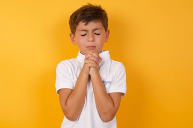 Sarı duvarda dua eden sevimli çocuk.  