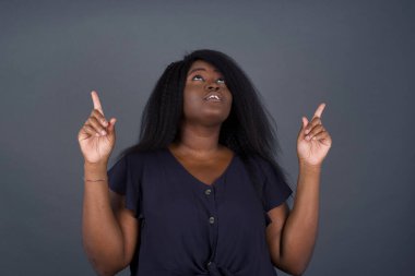 Başarılı Afro-Amerikan kadının yatay görüntüsü heyecanlı bir şekilde iki işaret parmağıyla işaret ederek boş bir fotokopi duvarında şok edici bir şey gösteriyor..