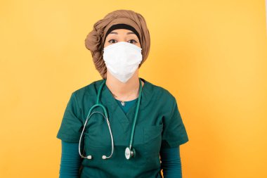 Hoş görünümlü, genç, Müslüman, yeşil üniformalı, dudaklarını öpecek gibi tutan, ifadesine sevinen, suratını buruşturan güzel bir doktor kadın. Kapalı yerde dikiliyorum. Güzellik konsepti.