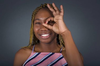 Güzel, gülümseyen, Afro-Amerikalı bir kadın el pençe divan duruyor. Gri stüdyo arka planındaki deliğe bakıyor.  