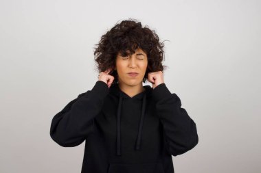 Bu sinir bozucu sesi çıkarmayı kes! Mutsuz, kapüşonlu, endişeli, kulaklarını parmaklarıyla tıkayan, üst katındaki komşulardan gelen gürültüden rahatsız olan genç bir kadının vesikalığı..