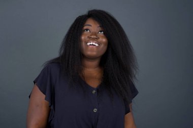 İnsanlar ve ani tepki kavramı. Şaşırmış Afrikalı Amerikalı kadın, omuz silkiyor, yana bakıyor, arkadaşlarıyla yeni planları için mutlu ve heyecanlı. Gri duvarda izole edilmiş..