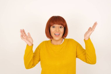 Neşeli kadın hoş bir jest yapıyor. Beyaz arka planda yalnız başına kollarını havaya kaldırıyor..