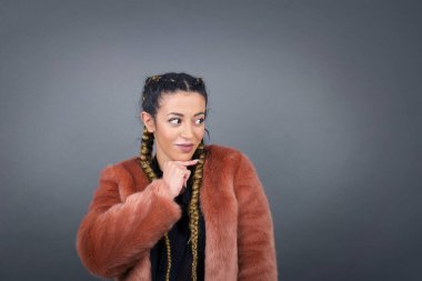 Hoş bir yüzü olan, günlük giysiler giyen, yan bakan, elini çenesinin altında tutan, hoş bir şeyler düşünen, gri arka planda poz veren hayalperest bir kadın..