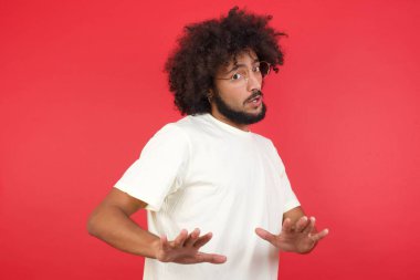 Afro saçlı genç adam kırmızı duvara karşı bir şeyi reddediyor.   