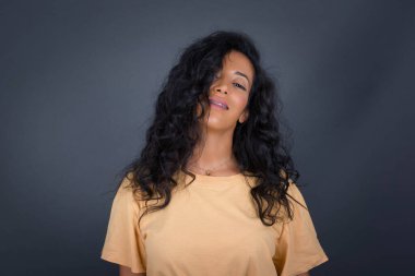 Hoş görünümlü esmer kadının yatay portresi. Yüzü uzun ve güzel, saçlarıyla kameraya mutlu bir şekilde bakıyor..